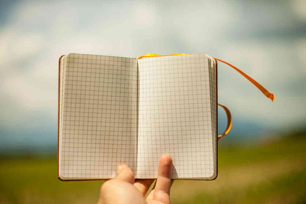 Open notebook with blank pages, held in hand.  Blurred outdoor background.